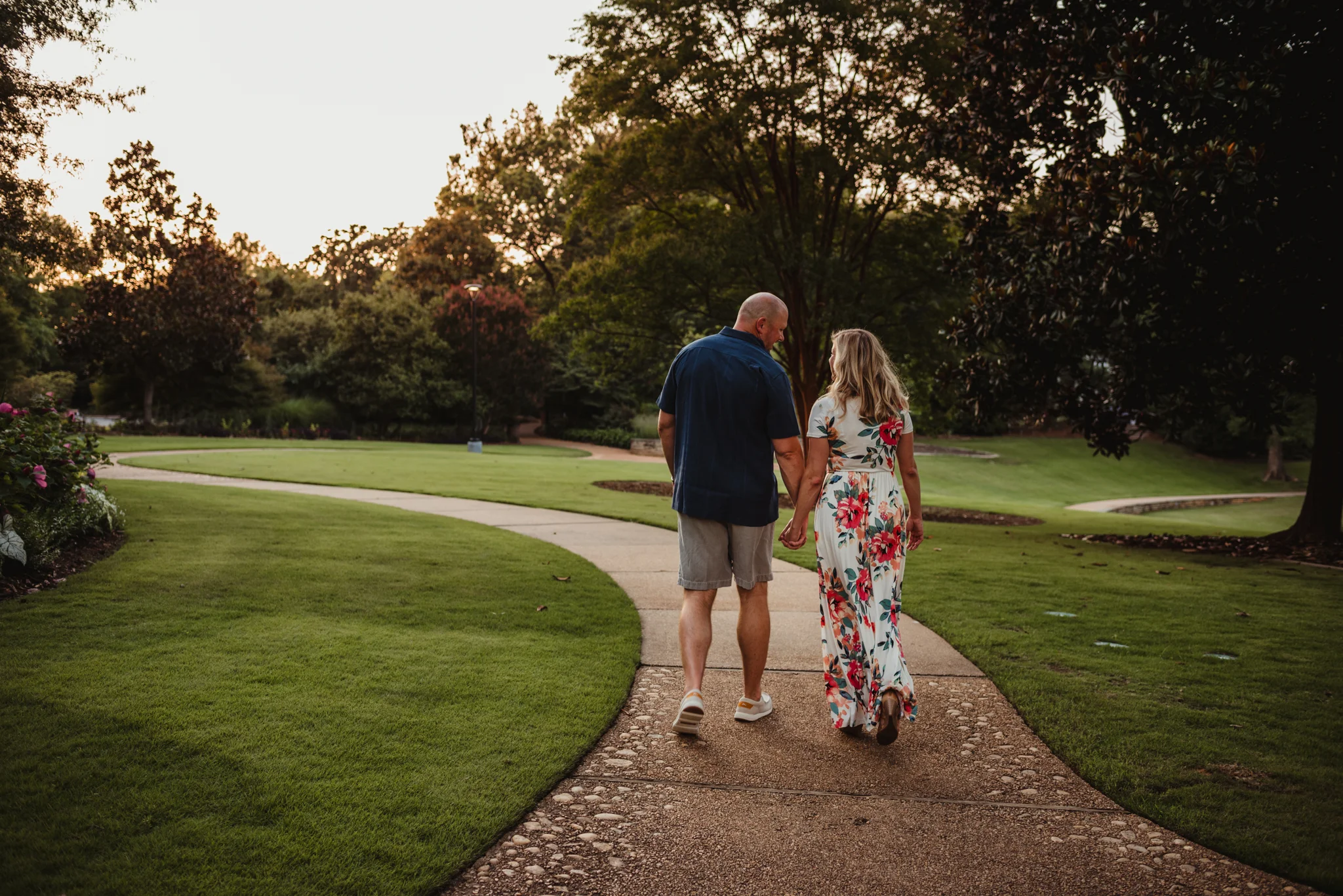 The bride and groom hold hands as they walk down the path during their engagement session at Fred Fletcher Park in Raleigh, North Carolina with Rose Trail Images.