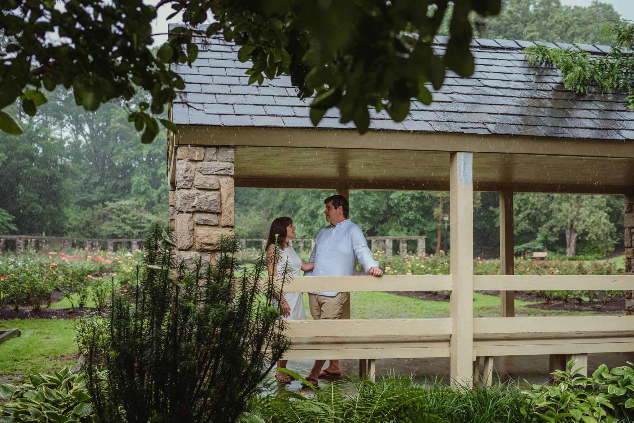 The bride and groom to be stand under the shelter during the rainstorm in Raleigh, during their engagement session with Rose Trail Images.