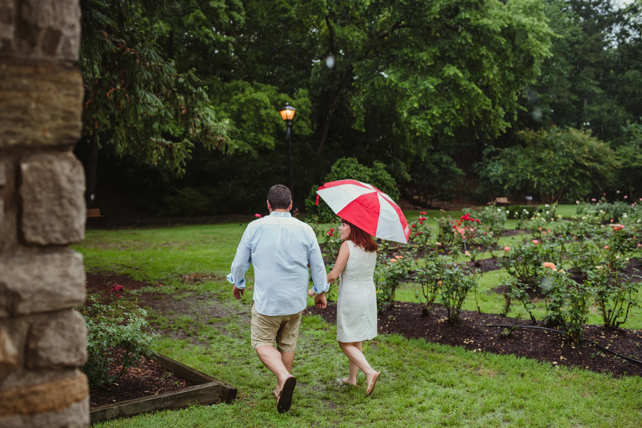 The bride and groom to be go walk under the umbrella during the rainstorm in Raleigh, during their engagement session with Rose Trail Images.