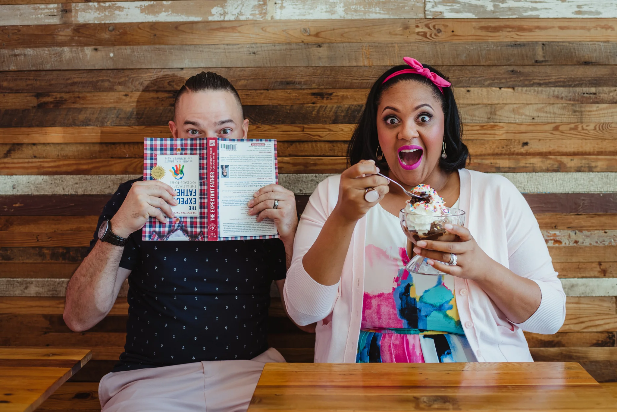 The parents to be eat a sundae and read a parenting book at The Parlour in Durham during their baby announcement photo session with Rose Trail Images.