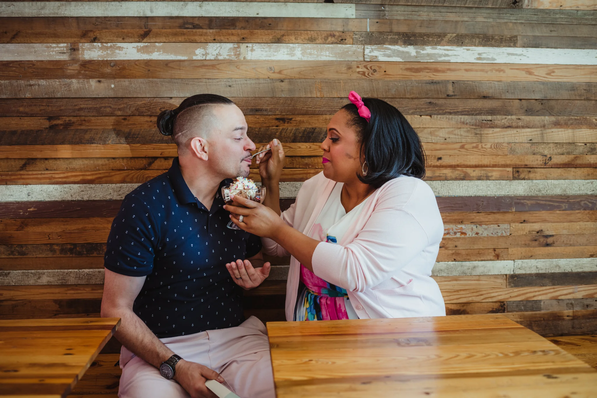 The mom to be feeds ice cream to the dad to be at The Parlour in Durham during their baby announcement photo session with Rose Trail Images.