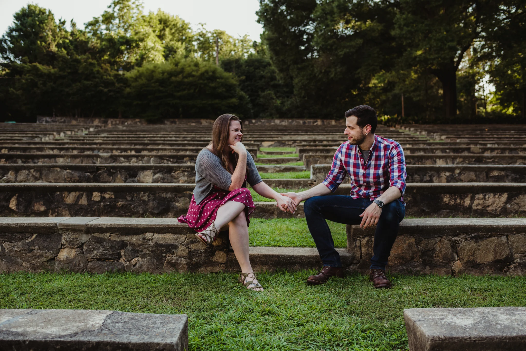The bride and groom to be sit and hold hands at the Little Theater at the Raleigh Rose Garden during their engagement session with Rose Trail Images.