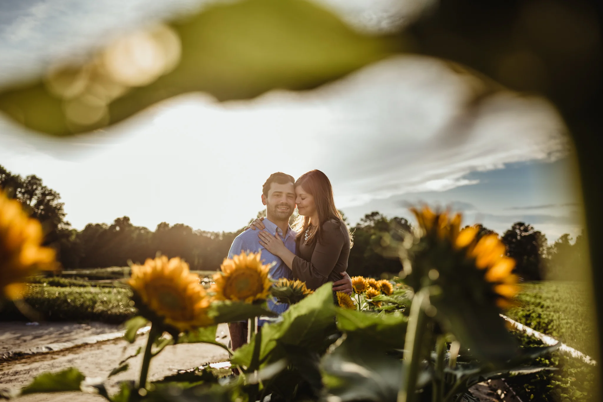 The bride and groom to be hold each other in the sunflowers for their engagement pictures with Rose Trail Images at their family farm in Benson, North Carolina.