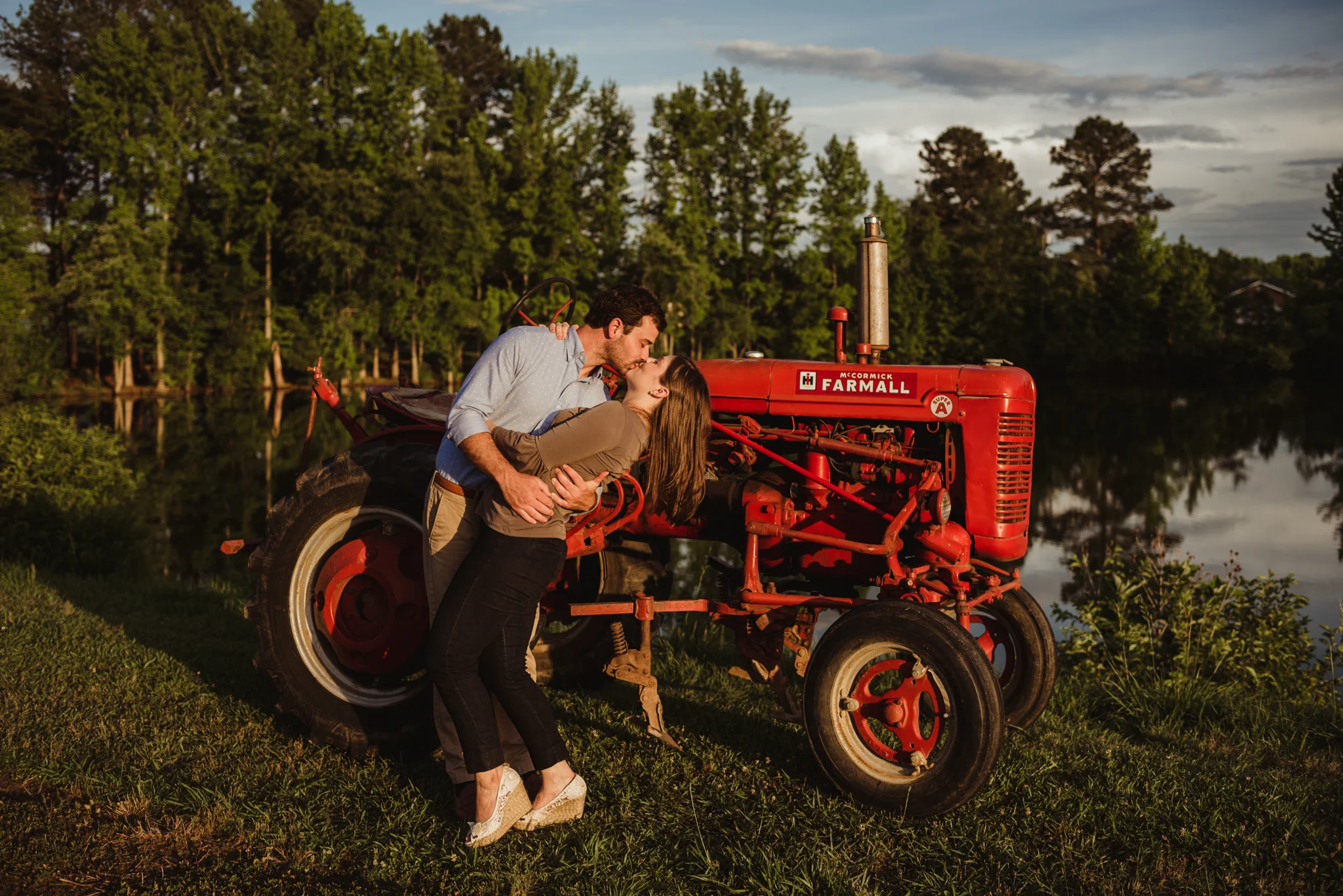 The bride and groom to be kiss in front of his grandfather’s tractor for their engagement pictures with Rose Trail Images at their family farm in Benson, North Carolina.