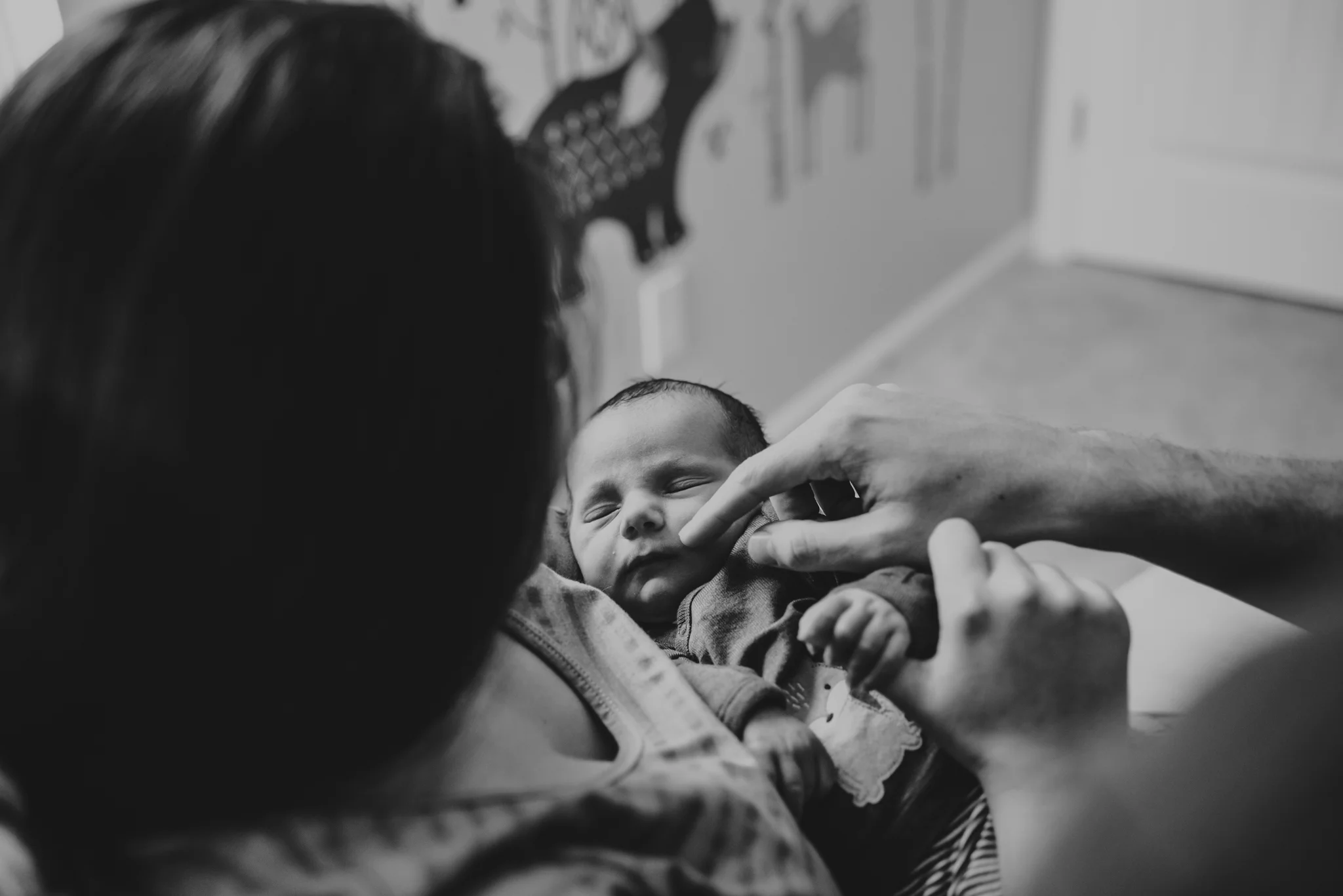 The new parents cuddle their son while holding him in his nursery in Wake Forest, a black and white image by Rose Trail Images.