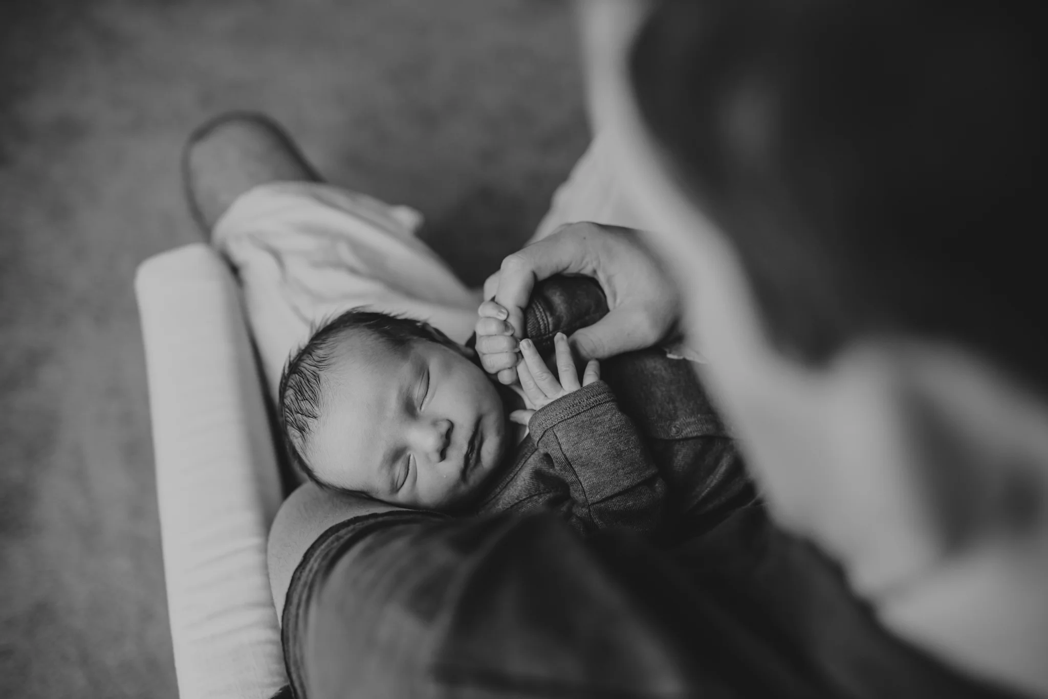The new Dad holds his newborn son’s hand in his nursery in Wake Forest, a black and white image by Rose Trail Images.