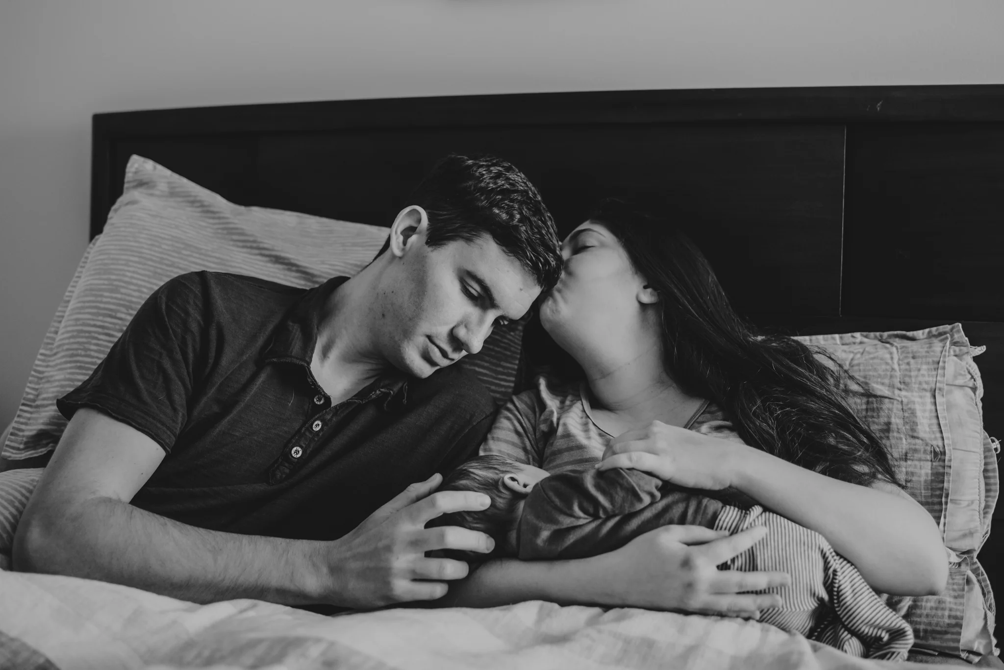 The new family snuggles with their newborn son in bed in Wake Forest, a black and white image by Rose Trail Images.