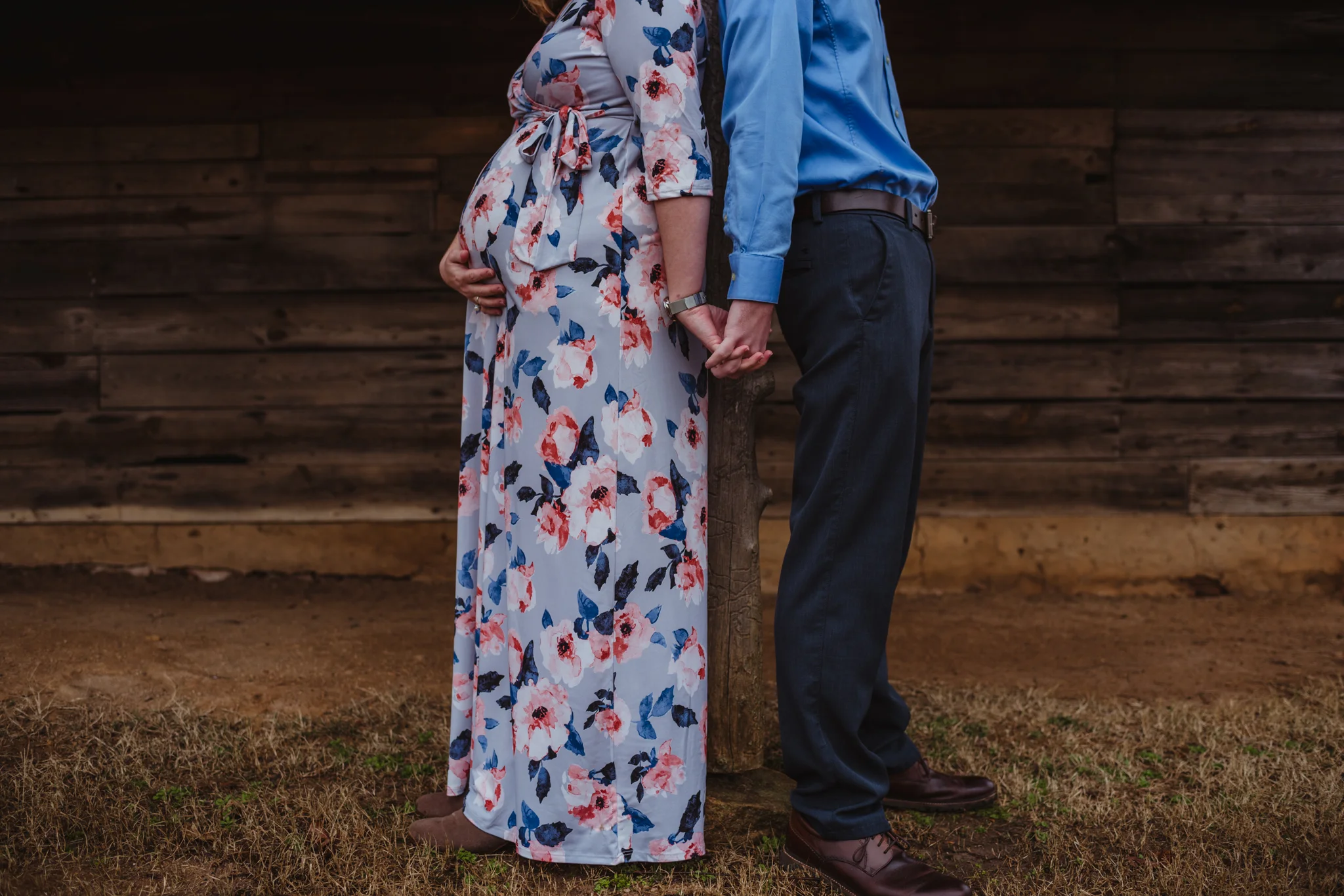 The parents to be hold hands and show off the baby bump under the old barn, picture taken by Rose Trail Images at Joyner Park in Wake Forest, NC.