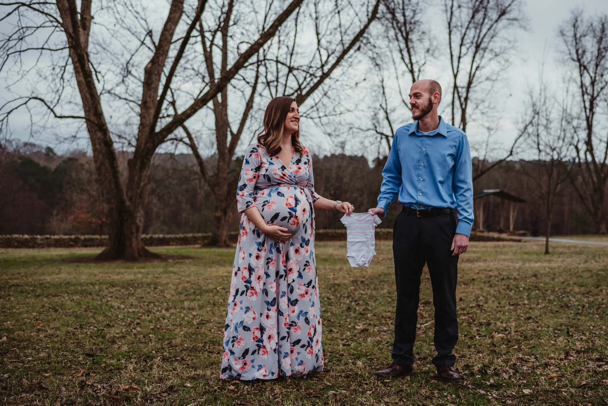 The parents to be show off her baby bump and some new onesies, picture taken by Rose Trail Images at Joyner Park in Wake Forest, NC.