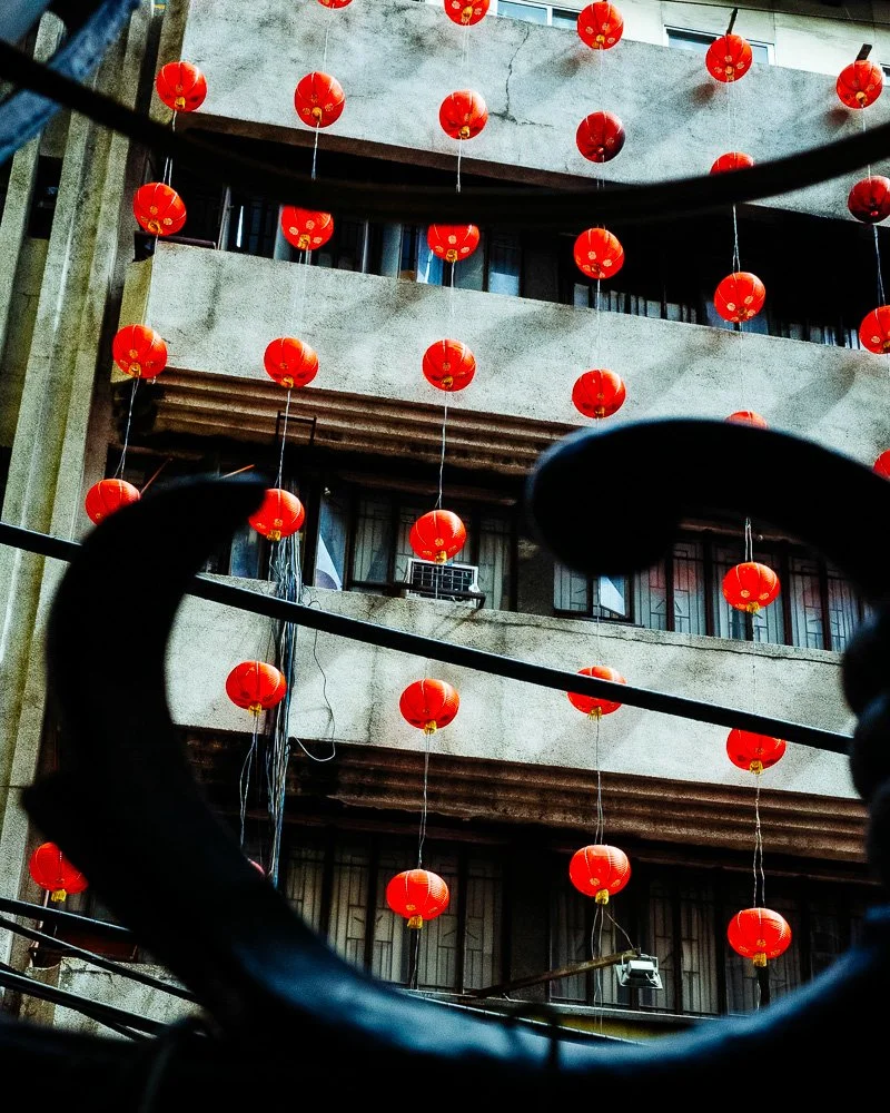 Red paper lanterns strung across the face of an apartment building, seen through curved railings
