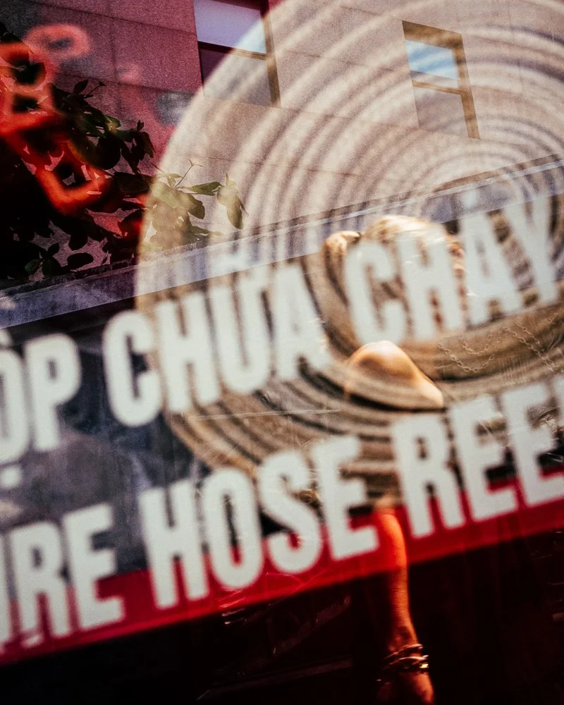 Reflection of a person in a conical hat over a red shop sign reading "fire hose reel"