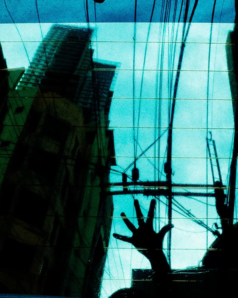 A hand pressed against a window reflecting high-rise buildings and tangled power lines