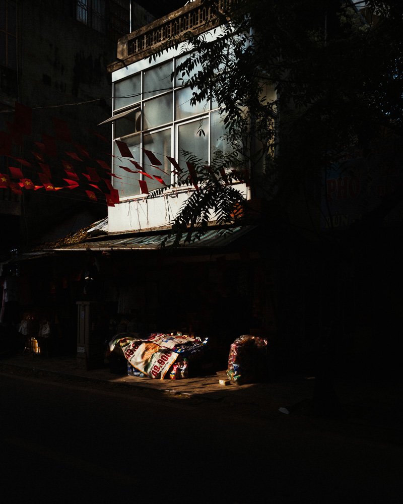 A shaft of light falling on a shopfront and bundles on a dark street
