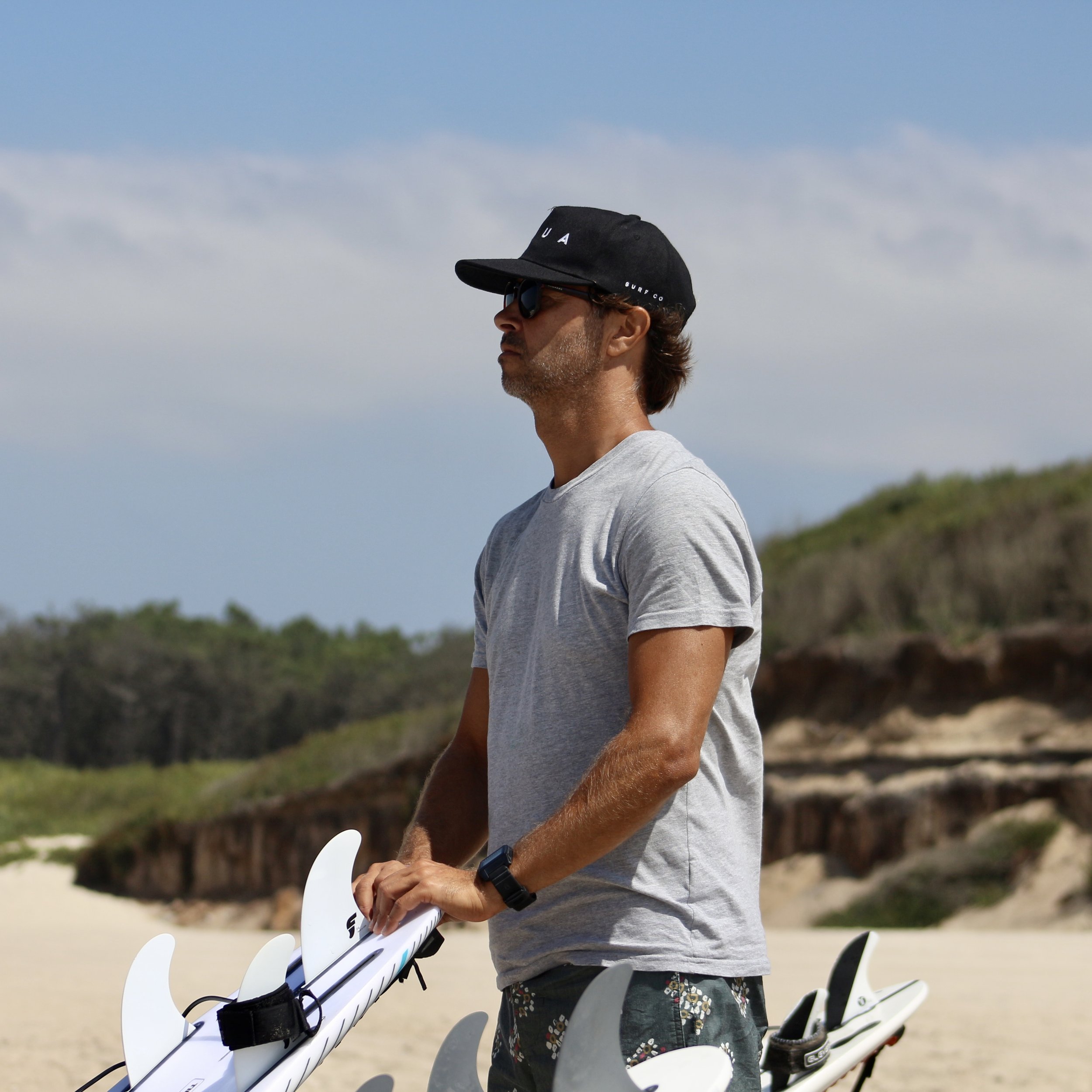 Head coach of B.SURF.PORTO standing on the beach with a surfboard, looking at the sea in Porto, Portugal
