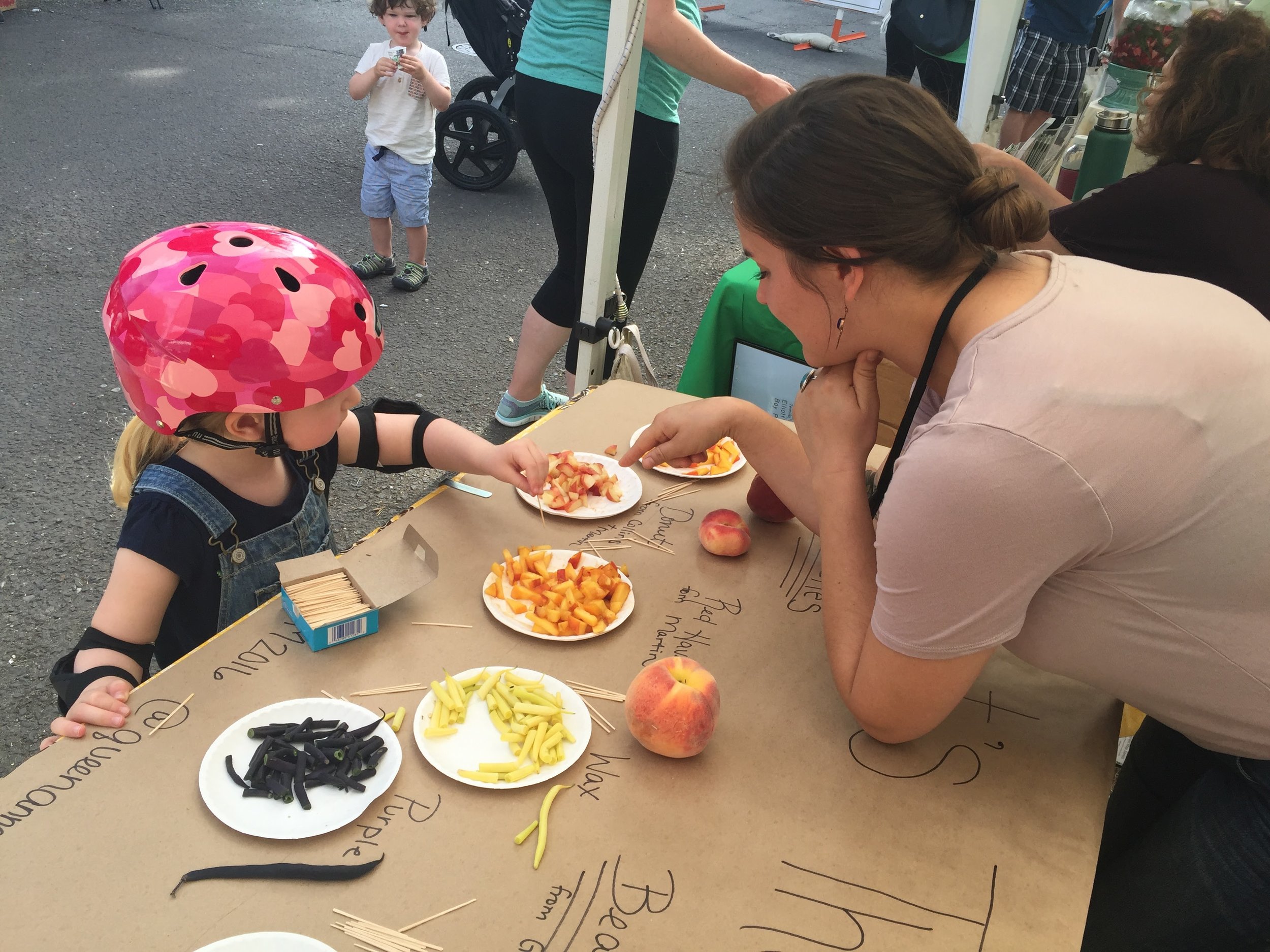 VOLUNTEER SARAH TASTE TESTS WITH A FRIEND AT THE EVENT TENT.