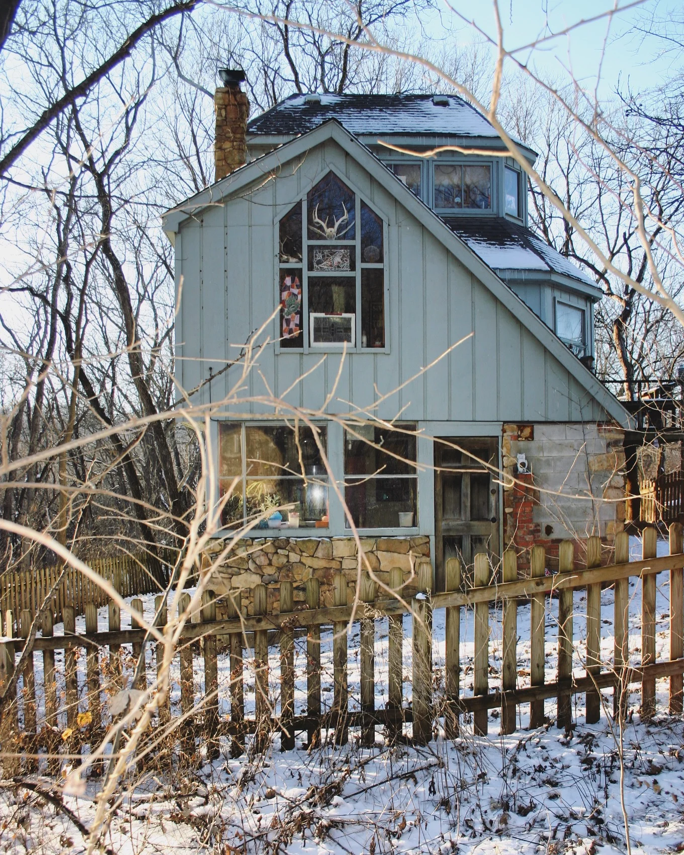 This is my favorite photo of the property because it shows how varied the elevations of the house of steps is. The wooden door is the entrance to the kitchen/first floor. The cathedral window with the antlers is the bedroom space. The window to the …