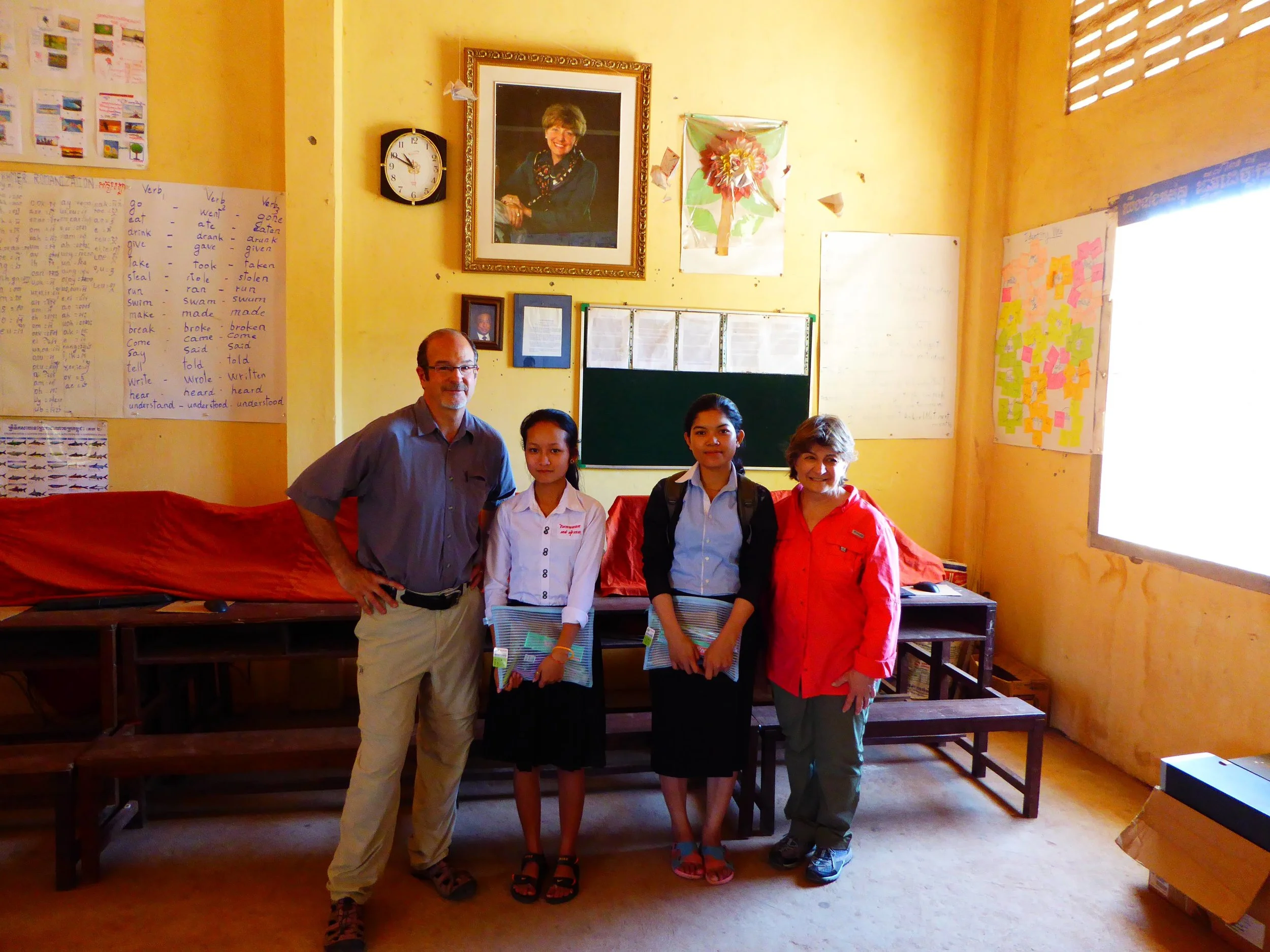 Founders Jim & Denise DeLong with Rachna and Pisey. Both had dropped out in 7th grade because of their families' poverty. We provided scholarships from 7th-12th grade and, with our continuing funding, both are now attending university. Doris Dillon's portrait is in the background.