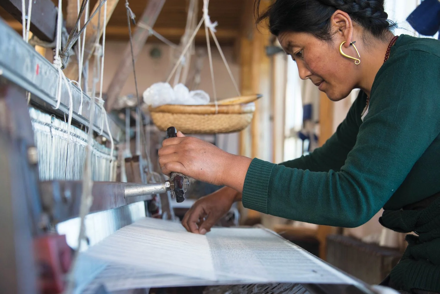 At the atelier in Tibet, an artisan uses a loom to make a yak wool scarf. 