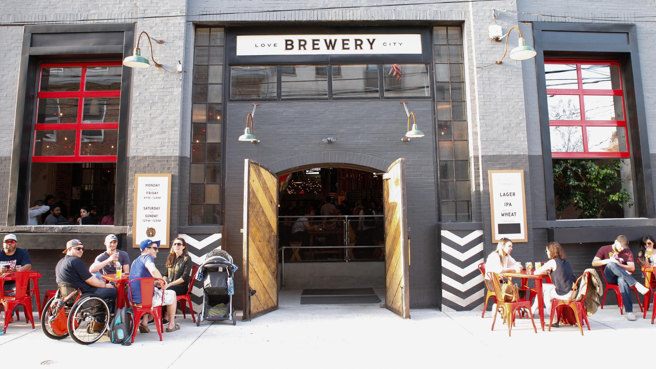  Love City Brewing taproom entrance featuring sidewalk seating and large open garage door-style windows. 