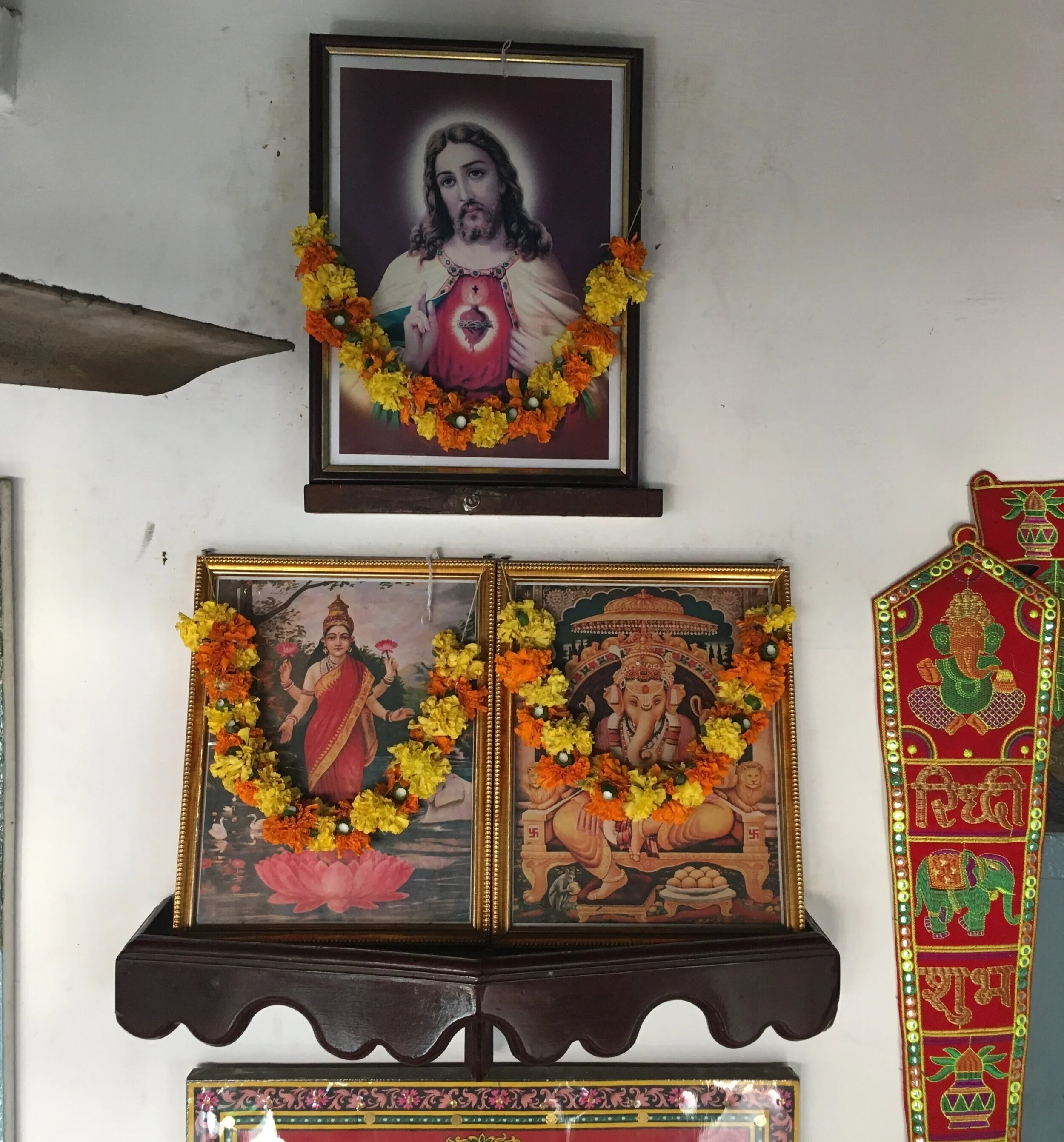 A picture of Jesus hangs above the icons of Hindu goddess Kali (left) and the god Ganesh (right) in a Christian-owned cafe in Kochi, Kerala, South India. The garlands, made of marigold flowers, are commonly offered in Hindu temples. Photo by Meagan Clark.