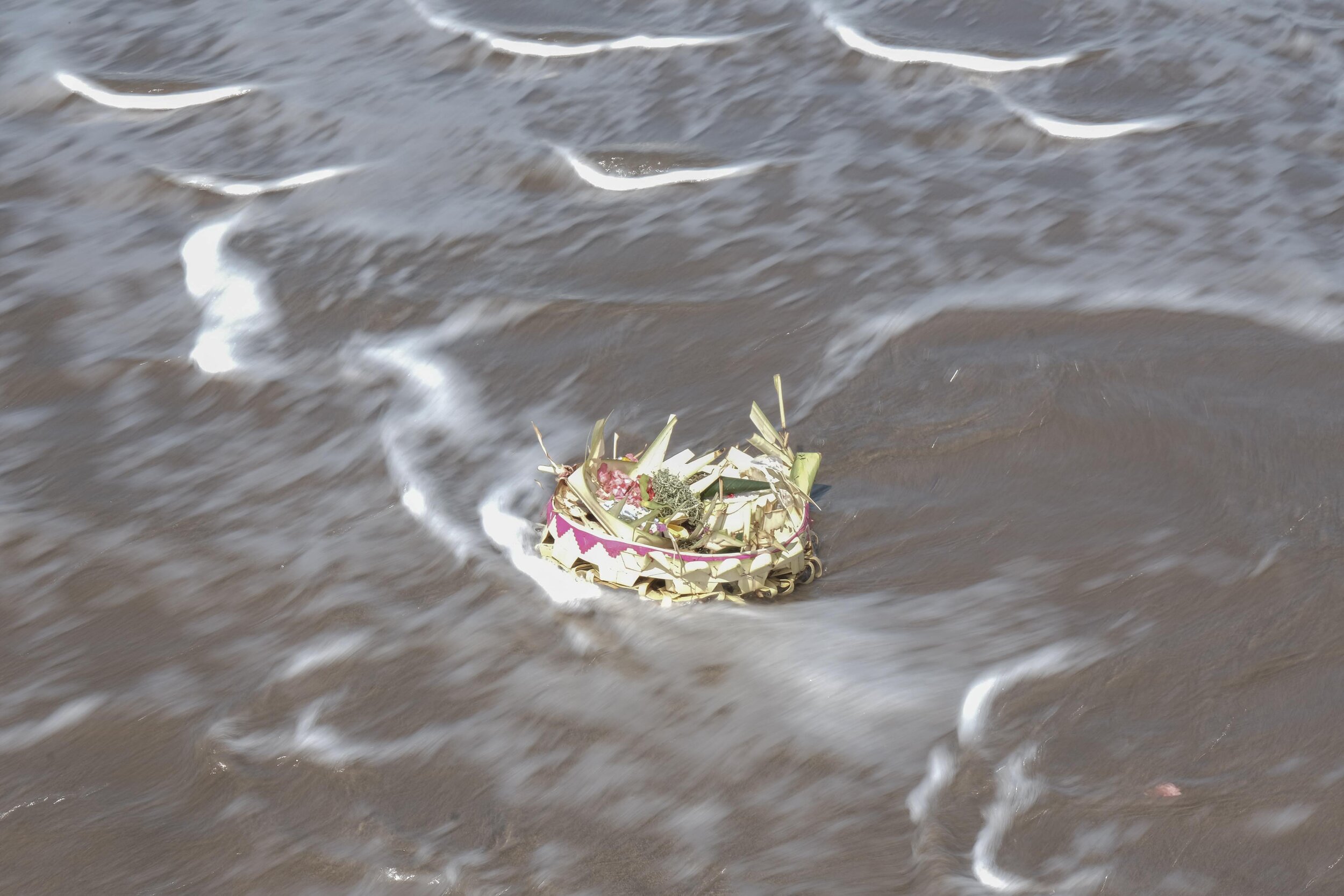  Offerings to the gods consisting of flowers and fruit are swept away by waves of seawater. Photo by Agoes Rudianto. 