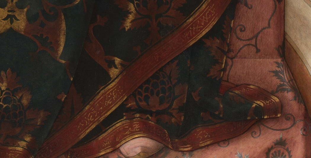 A close up of Mary's slippered feet. The hem of her robes are red with gold inscriptions.