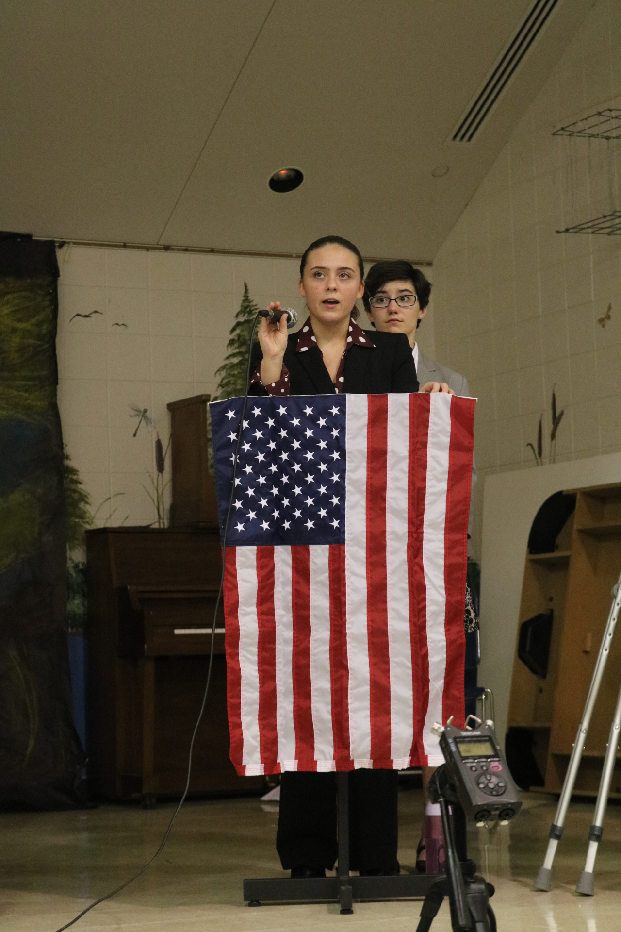 student speaking behind podium with American flag