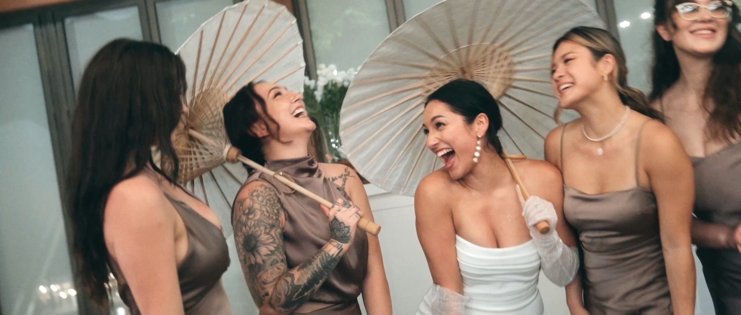 The bride and her bridesmaids smiling, holding parasols together in a joyful moment.