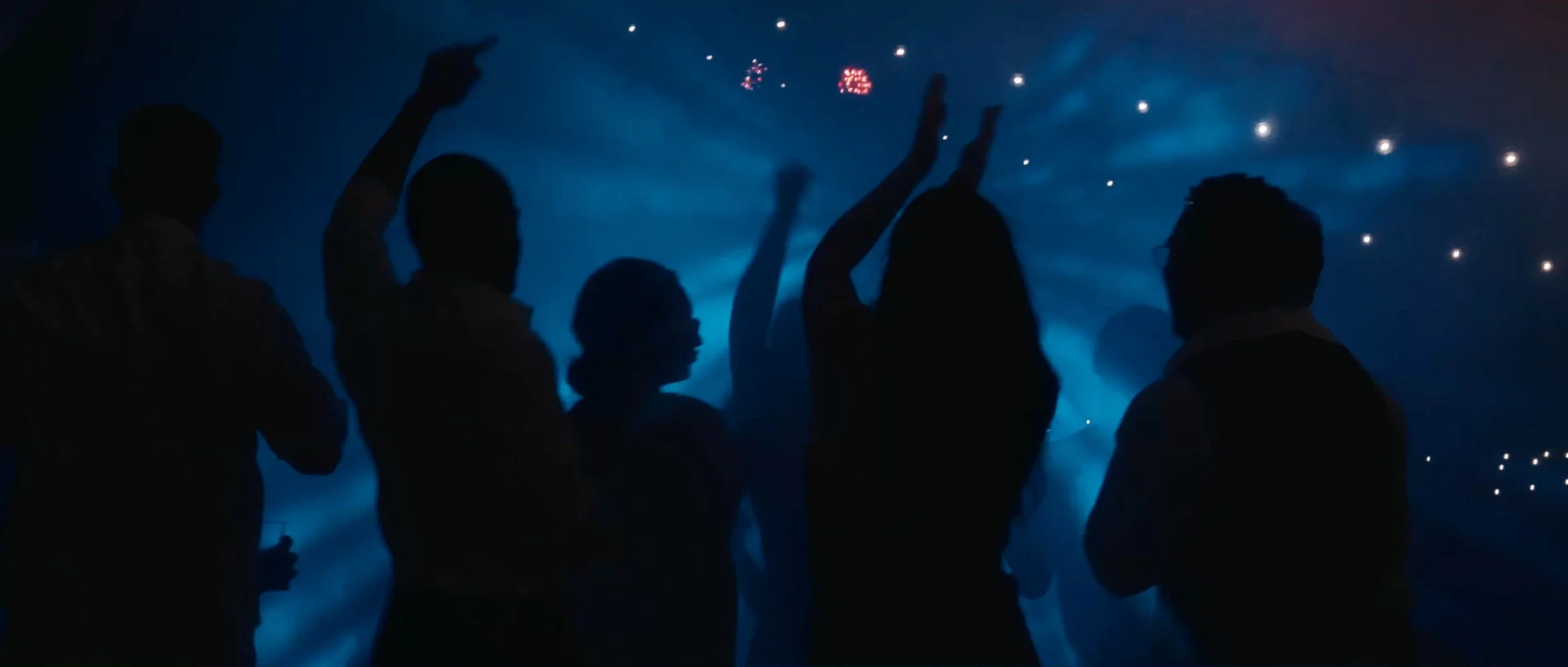 Silhouettes of guests dancing amidst fog and colorful lights at the wedding reception.