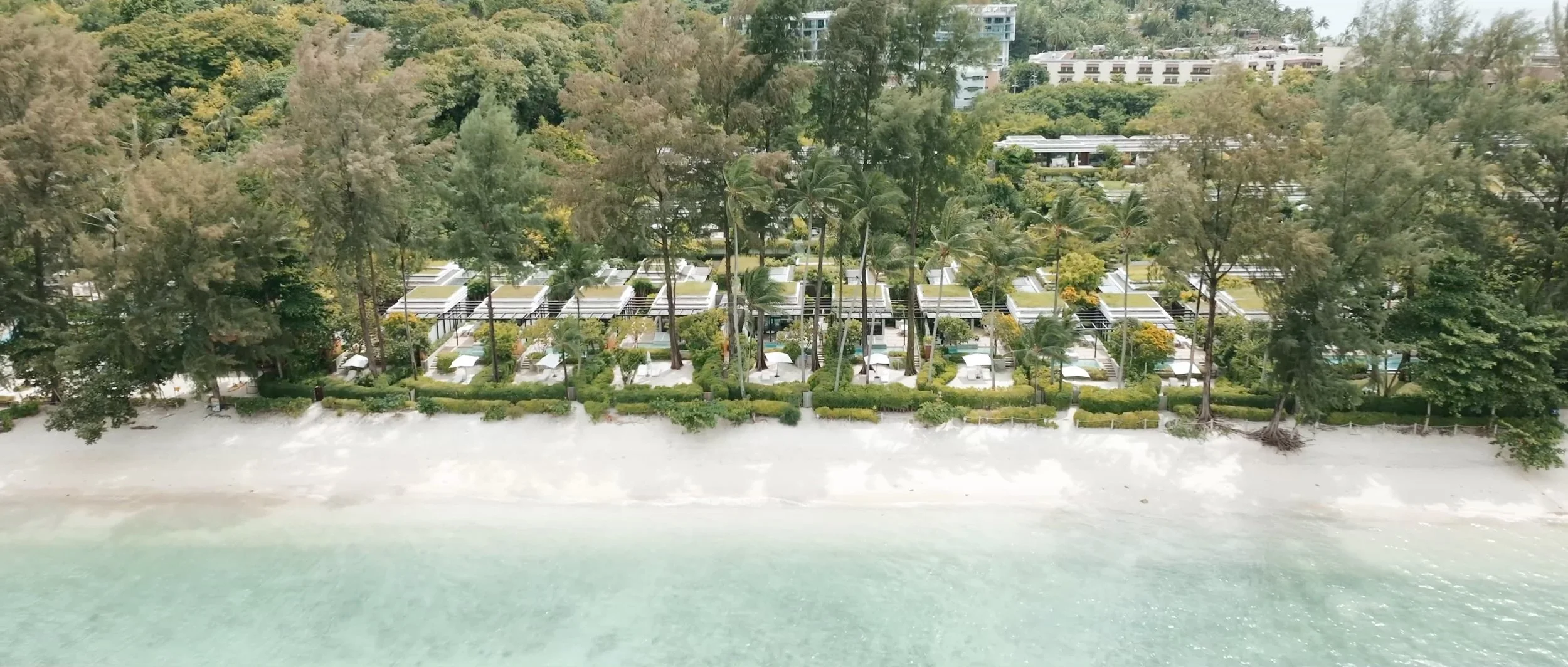 A drone shot of the Rosewood Phuket beachfront suites, nestled along the shoreline with turquoise waters in view.