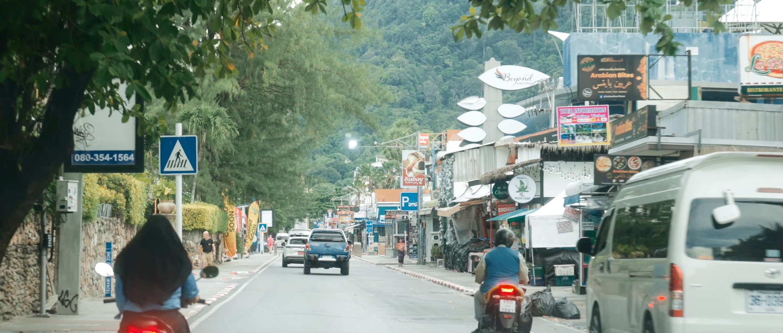 A street scene in Patong, Thailand, with motorbikes and shops lining the road, capturing the lively local atmosphere