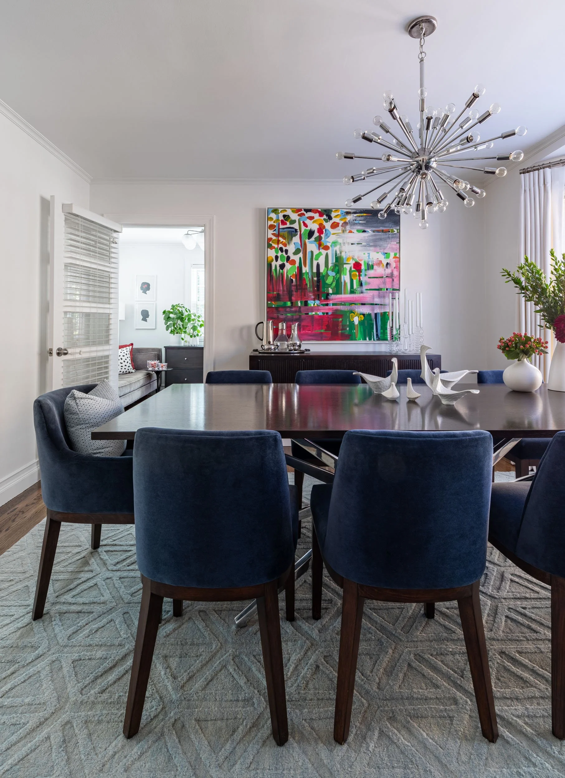Modern dining room in Edgebrook, Chicago, IL featuring a dark wood dining table, blue velvet chairs, and a custom area rug. Design by Wendy Nobriga Interiors.