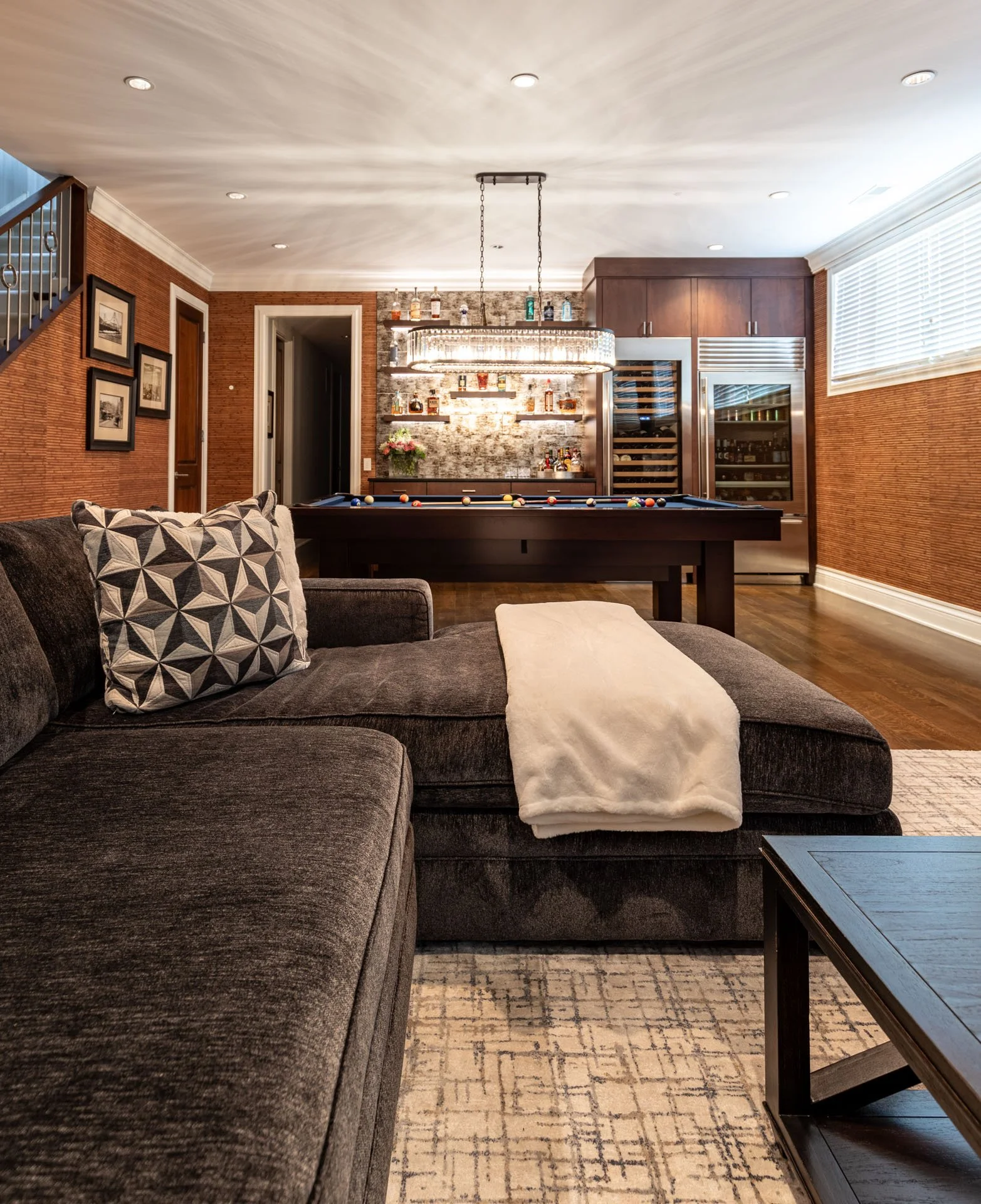 Reverse view from sectional toward pool table, bar, and chandelier in Roscoe Village Chicago basement, designed by Wendy Nobriga Interiors.