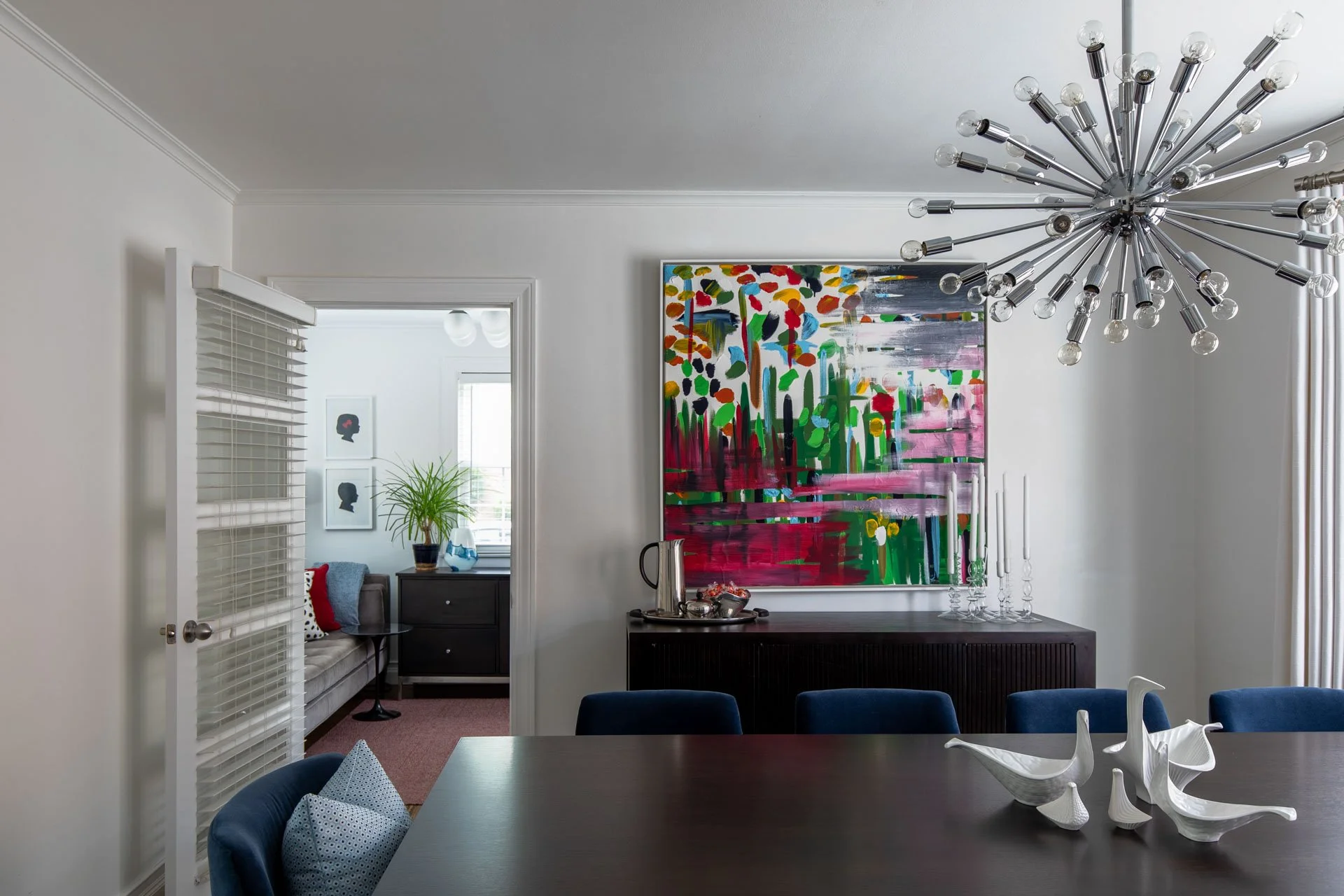 Dining room in Edgebrook, Chicago, IL with a vibrant painting above a sideboard, navy dining chairs, and a sculptural chandelier. Design by Wendy Nobriga Interiors.