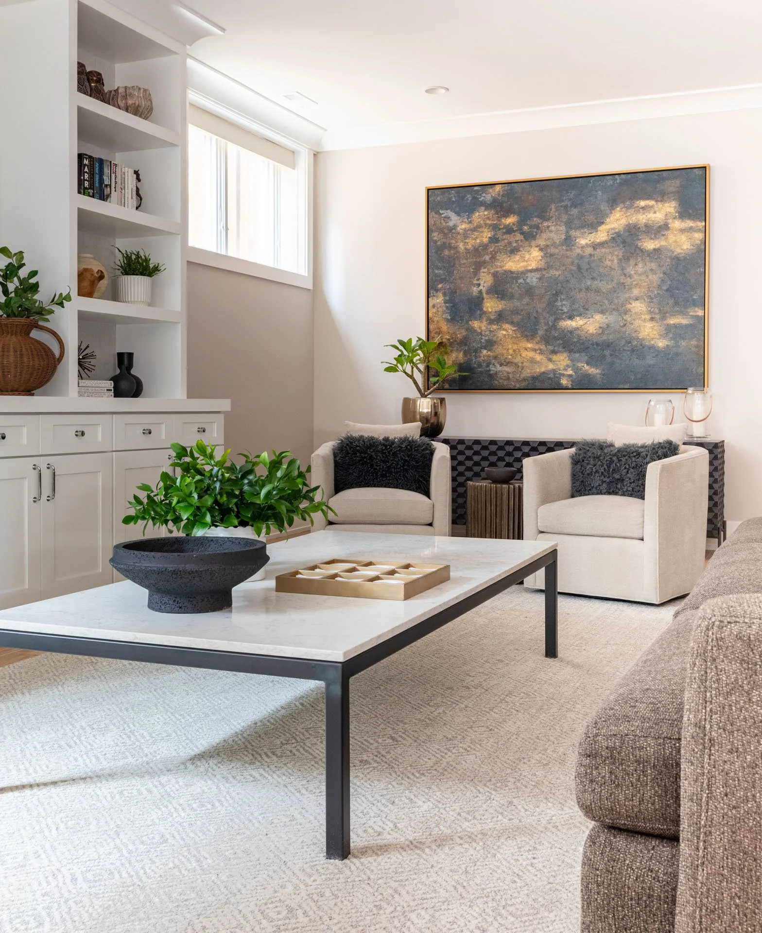 Detail of Roscoe Village Chicago basement family room featuring marble coffee table with greenery, upholstered armchairs, and abstract artwork, designed by Wendy Nobriga Interiors.
