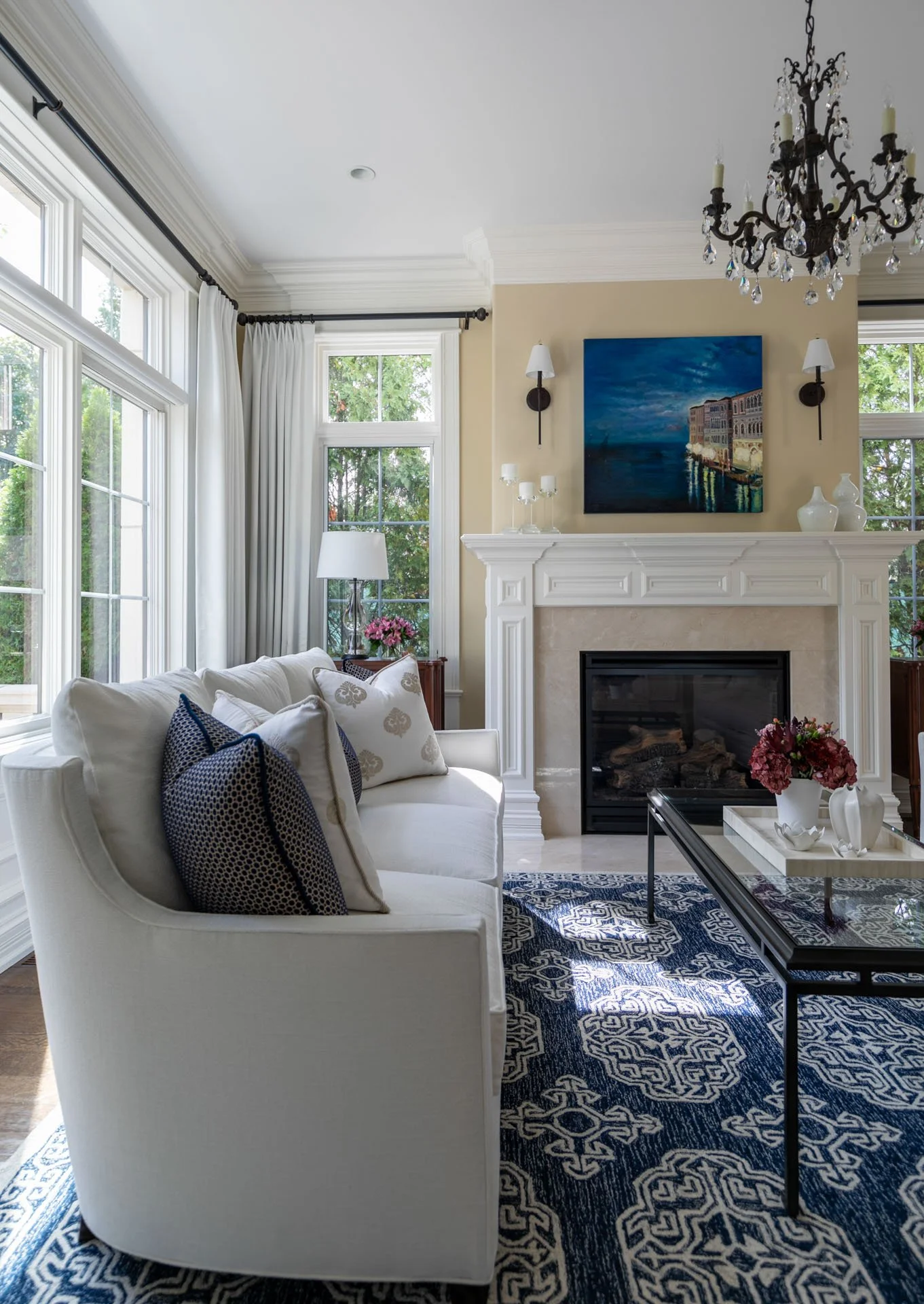 Elegant Lincolnwood IL living room with white sofa, fireplace mantel, navy rug, and chandelier, designed by Wendy Nobriga Interiors.