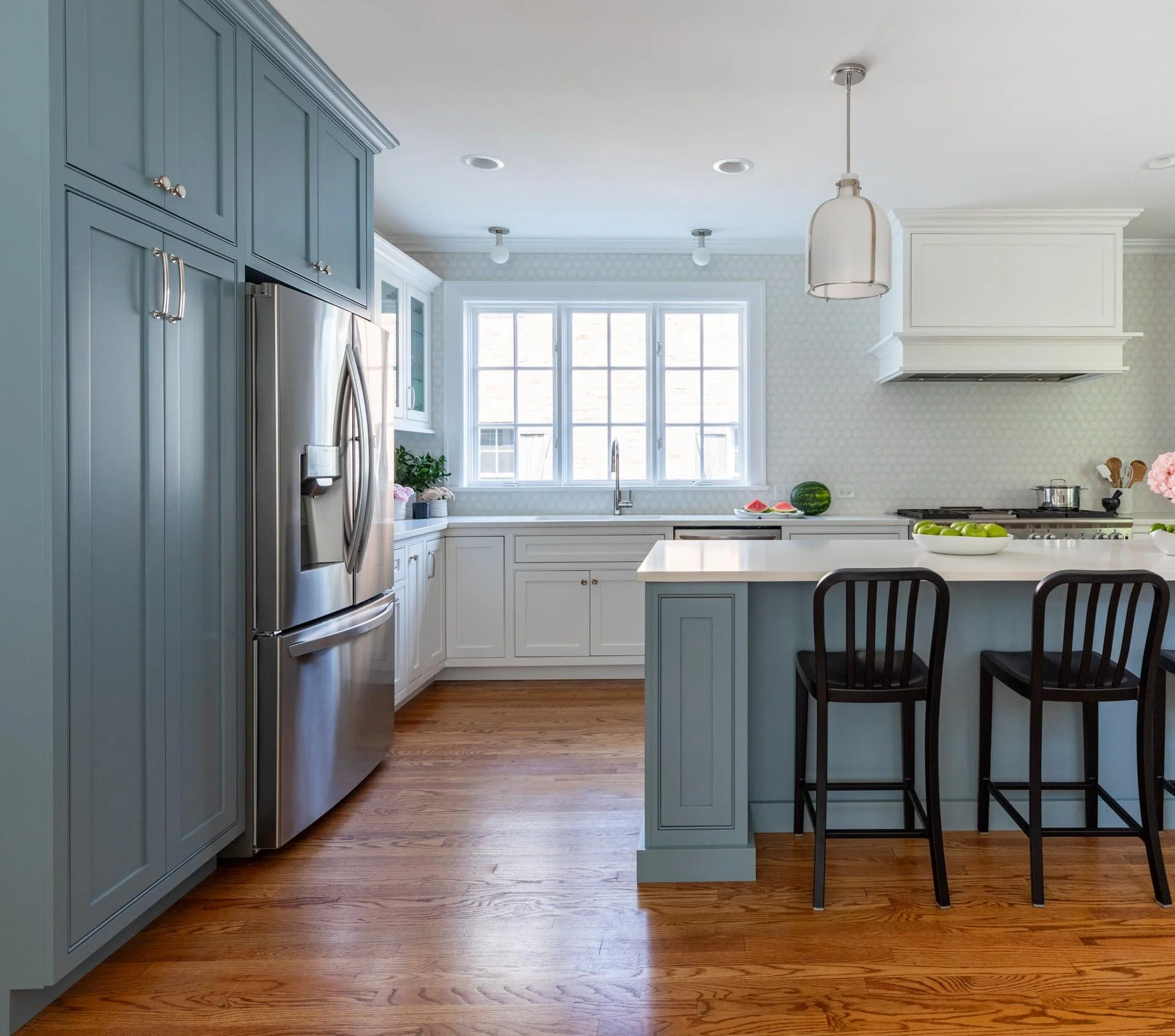 Lake Forest IL transitional kitchen with a large blue island featuring open shelving for cookbooks, white cabinets, stainless steel appliances, and pendant lighting, designed by Wendy Nobriga Interiors.