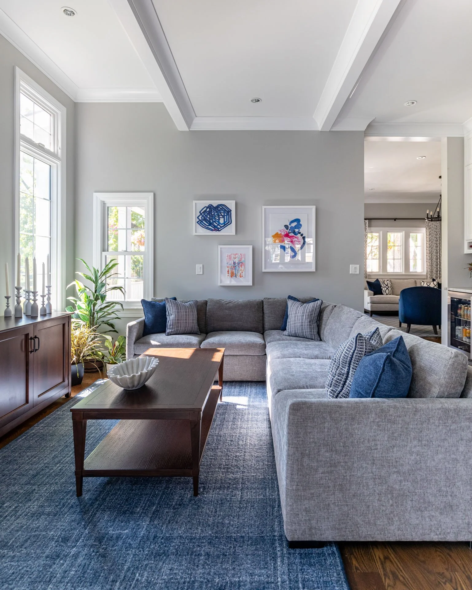 La Grange, IL family room with gray sectional sofa, blue accent pillows, modern artwork, and wood coffee table, designed by Wendy Nobriga Interiors