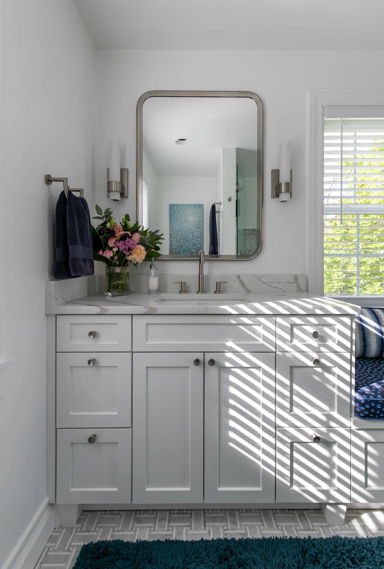 Straight-on view of primary bathroom vanity with quartz countertop, modern mirror, brushed nickel sconces, and navy towels, Edgebrook, Chicago, IL, designed by Wendy Nobriga Interiors.