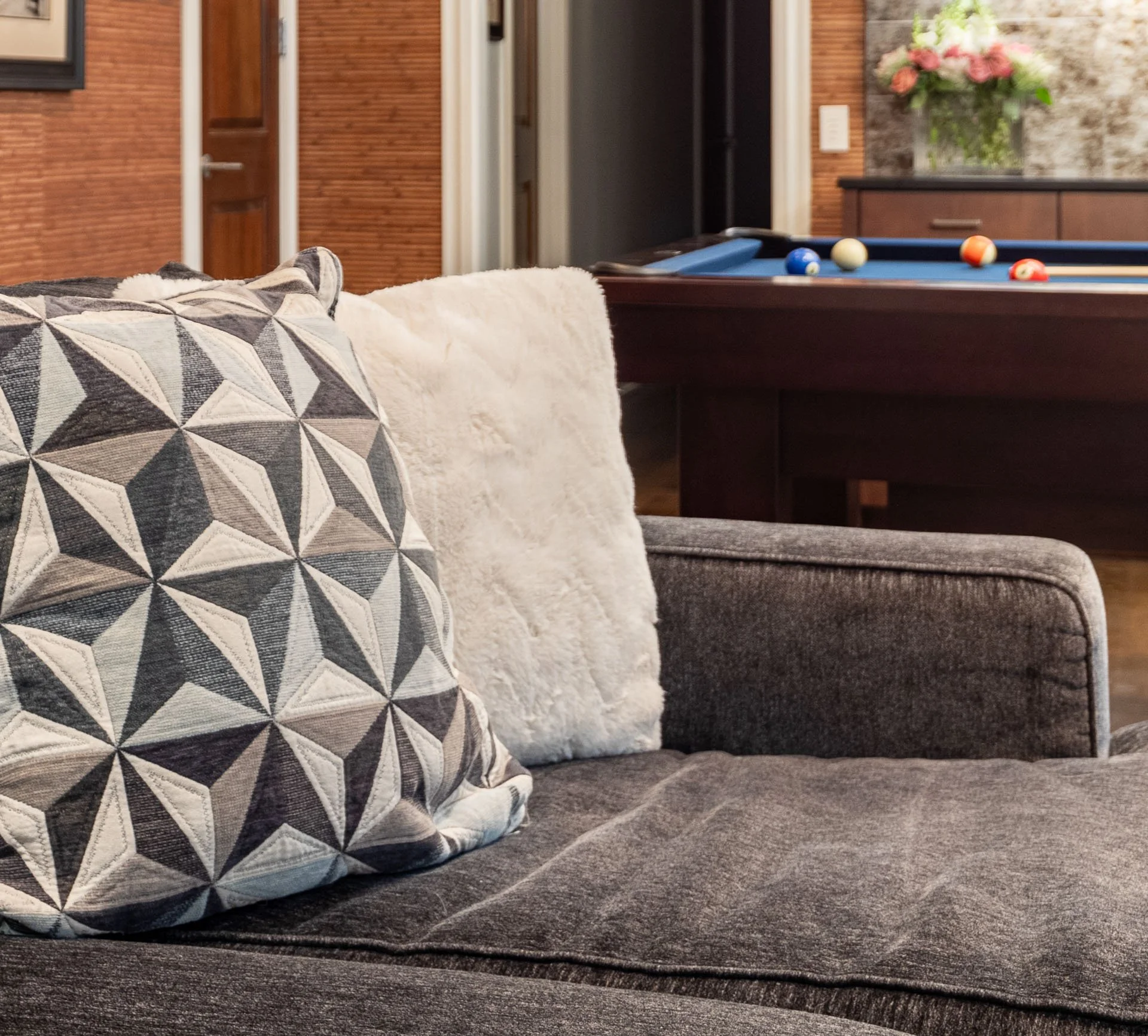 Detail of geometric accent pillow on gray sectional sofa with pool table in background in Roscoe Village Chicago basement, designed by Wendy Nobriga Interiors.