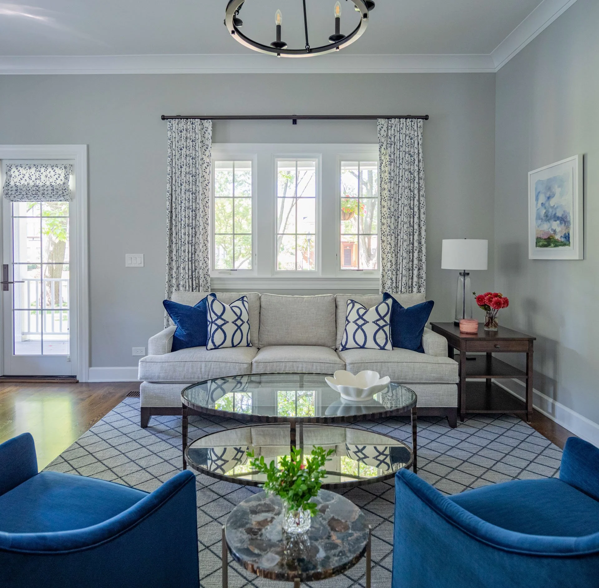 La Grange IL living room with light gray sofa, navy chairs, round glass coffee table, and patterned drapery designed by Wendy Nobriga Interiors