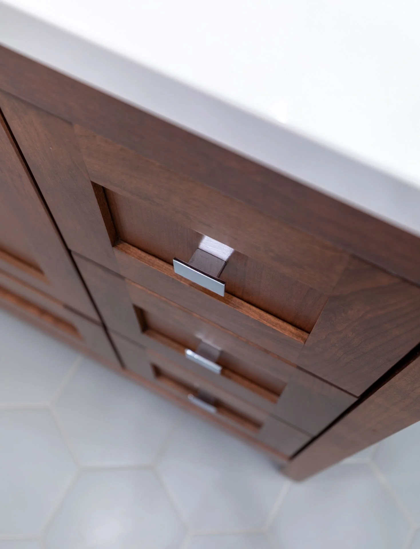 Lake View Chicago primary bathroom detail of wood vanity drawers with chrome hardware, white quartz countertop, and gray hexagon tile floor, designed by Wendy Nobriga Interiors