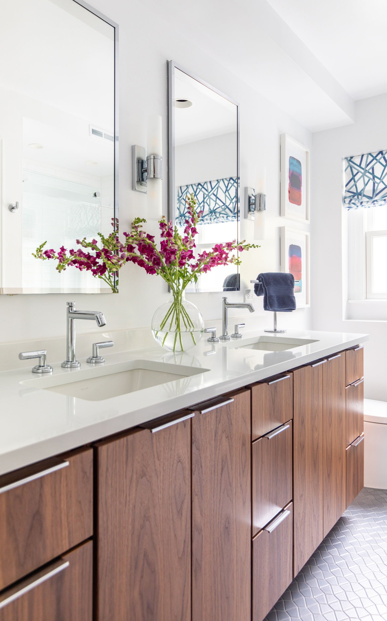 Kids bathroom double vanity in Northbrook, Illinois with walnut cabinetry, integrated sinks, chrome fixtures, and modern wall sconces. Design by Wendy Nobriga Interiors.