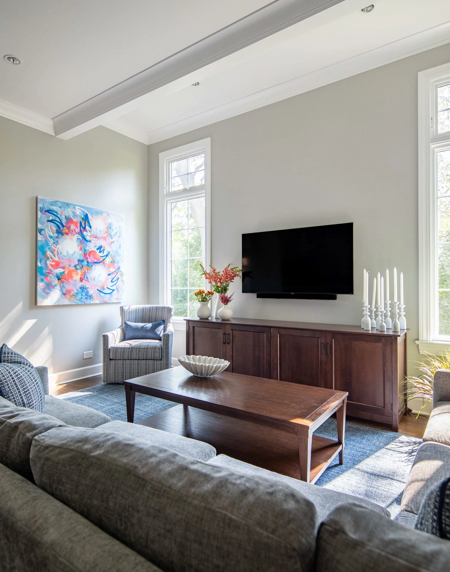 La Grange, IL family room featuring a gray sectional sofa, accent chair, TV wall, and vibrant modern artwork, styled by Wendy Nobriga Interiors.