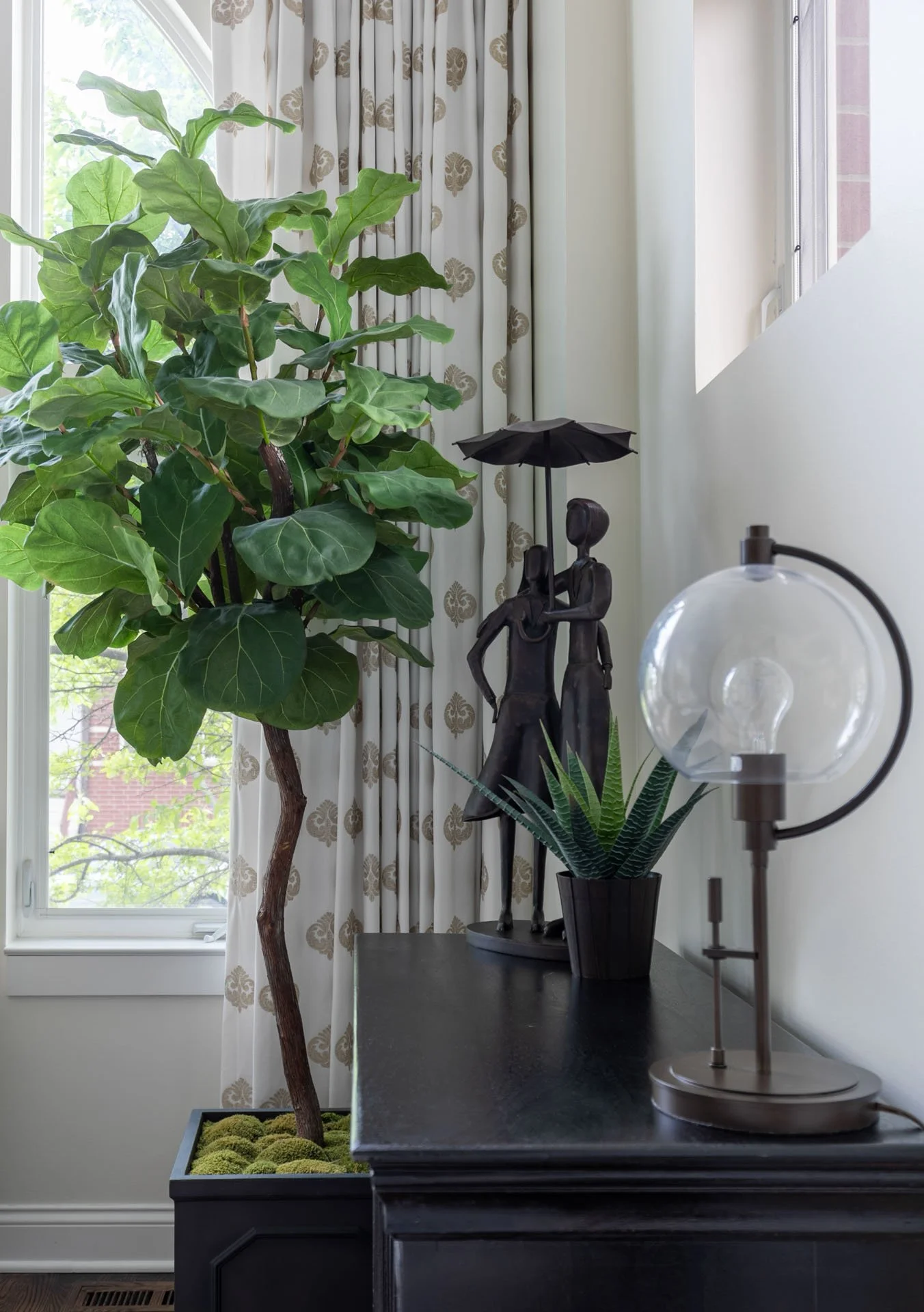 Des Plaines IL living room vignette with fiddle leaf fig, sculptural figurine, glass lamp, and patterned drapery by Wendy Nobriga Interiors