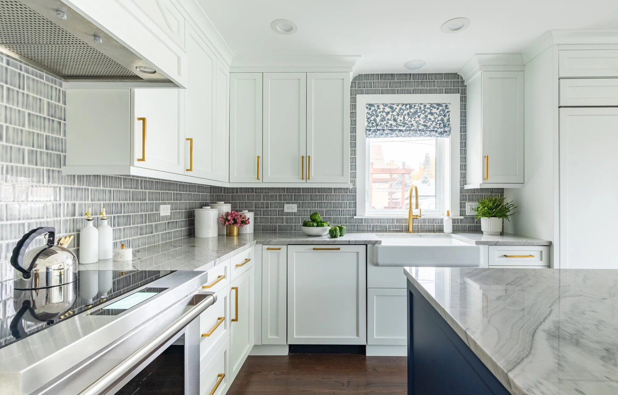 Bright white kitchen in a North Edgebrook Chicago home featuring custom cabinetry, a farmhouse sink, blue textured tile backsplash, quartzite countertops, and brass fixtures, designed by Wendy Nobriga Interiors.