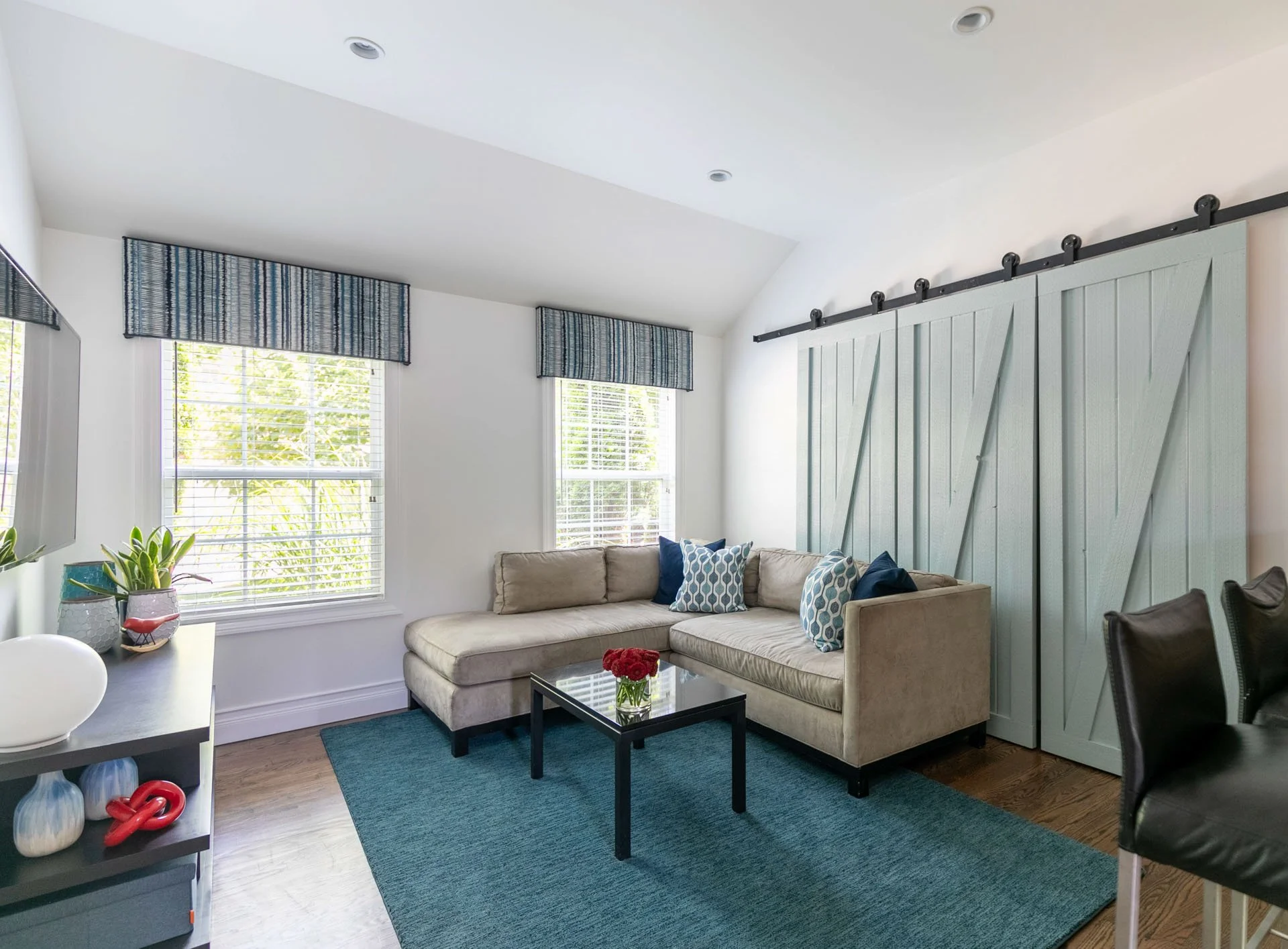 Family room in Edgebrook, Chicago, IL featuring a beige sectional sofa with blue accent pillows, teal area rug, and sliding barn doors designed by Wendy Nobriga Interiors.