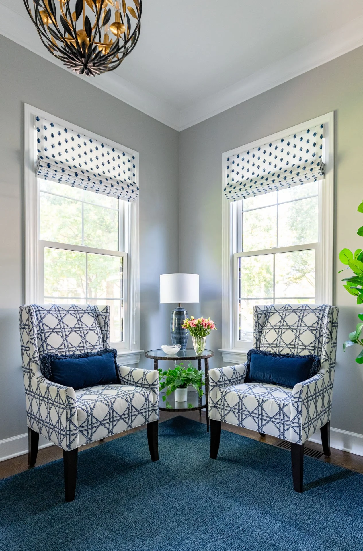 La Grange foyer corner with patterned accent chairs, blue rug, side table with flowers, and layered roman shades, design by Wendy Nobriga Interiors.