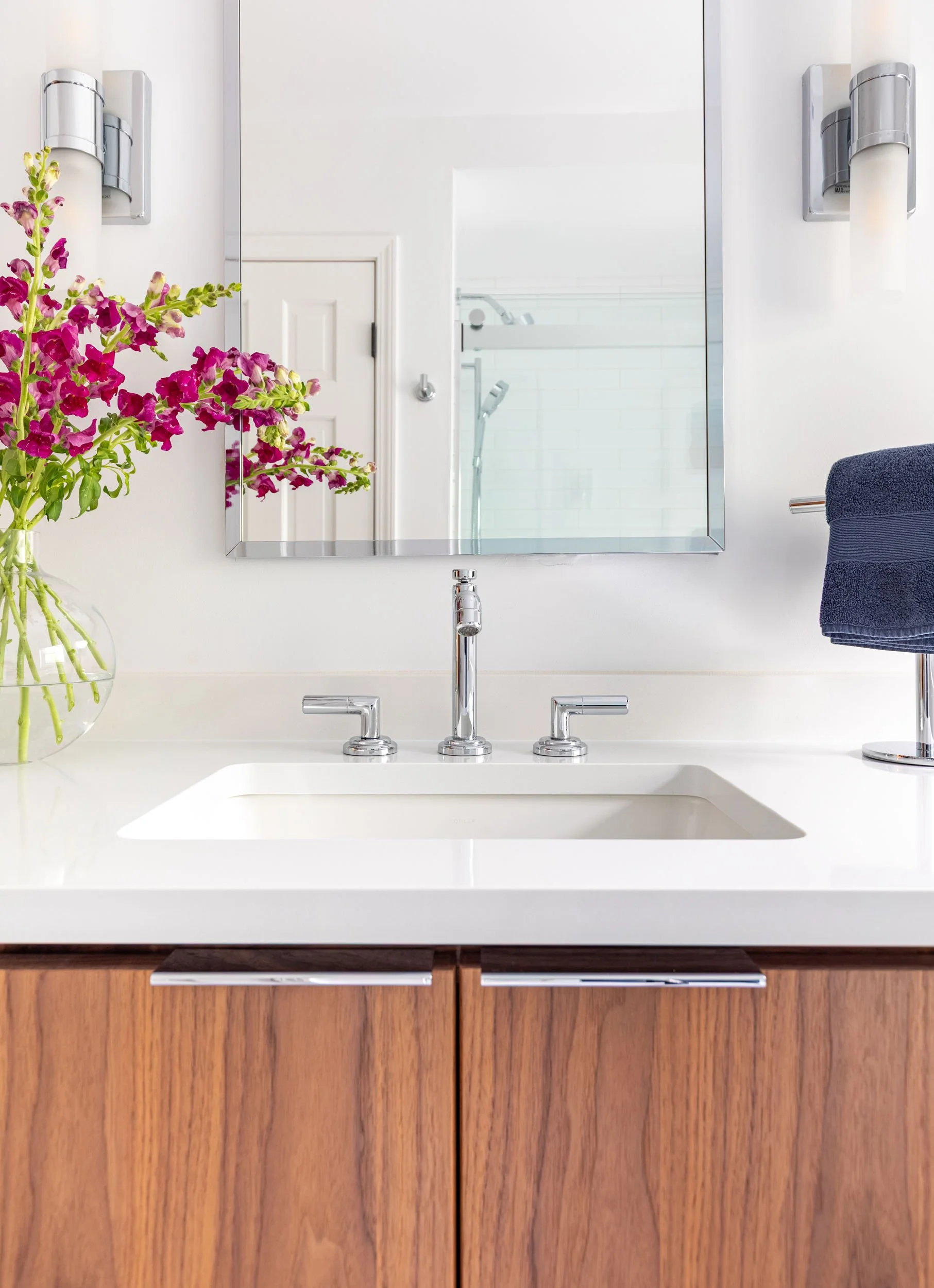 Kids bathroom vanity in Northbrook, Illinois with walnut cabinetry, integrated sink, chrome fixtures, and modern wall sconces. Design by Wendy Nobriga Interiors.