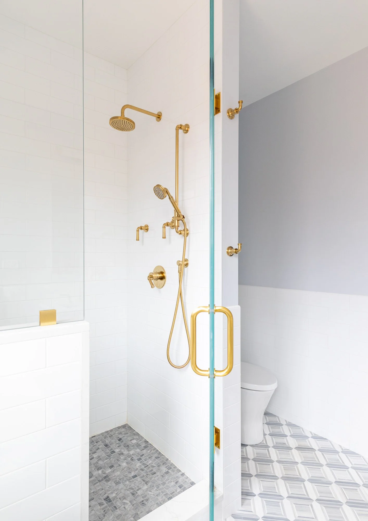 Walk-in shower in a North Edgebrook Chicago primary bathroom featuring a frameless glass enclosure, large-format wall tile, marble mosaic flooring, and brass shower fixtures, designed by Wendy Nobriga Interiors.